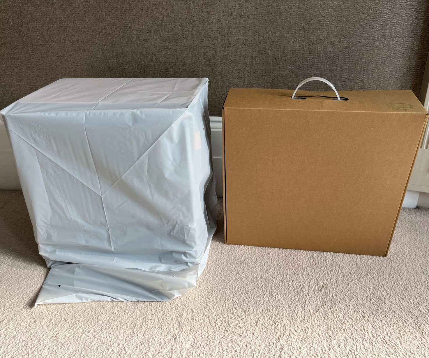 Two iRobot Roomba Combo j9+ boxes side by side, one cardboard and one with protective sleeve on cream carpet in front of brown wall in Alex's home