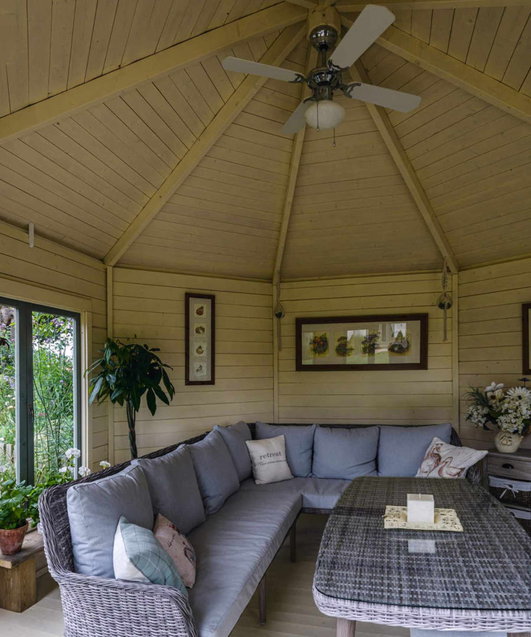 A sun room with a large L shaped rattan sofa and a ceiling fan