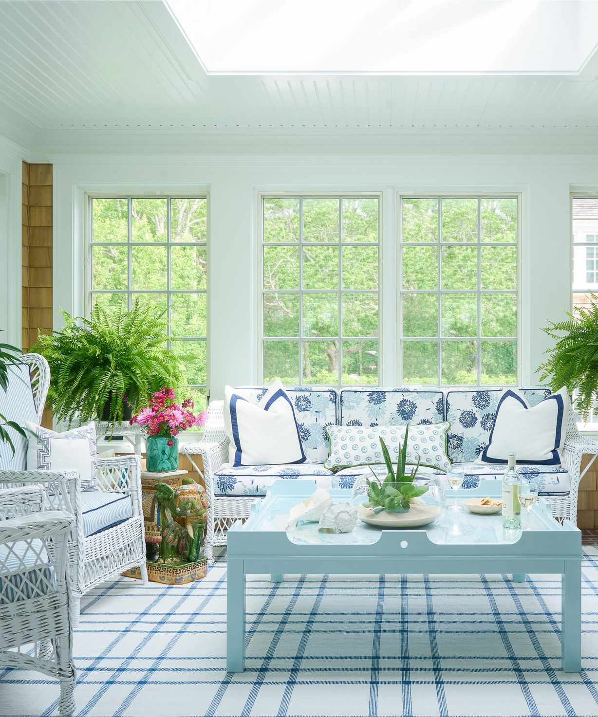 A coastal living room with wicker furniture, large windows and a vintage couch