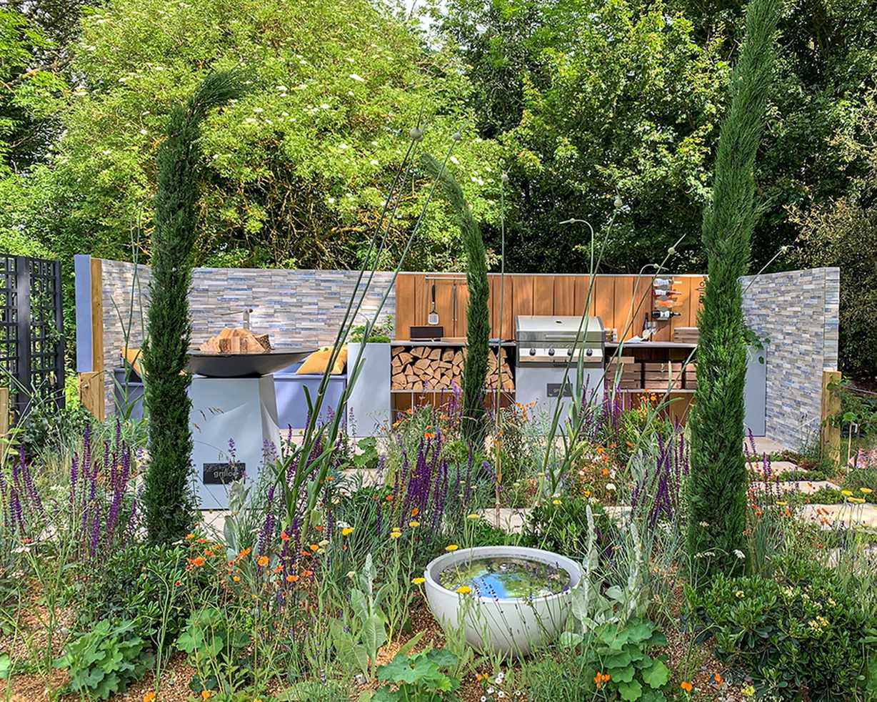 How much does an outdoor kitchen cost, explained with a slate-backed design featuring barbecue, fire pit and tall plants.