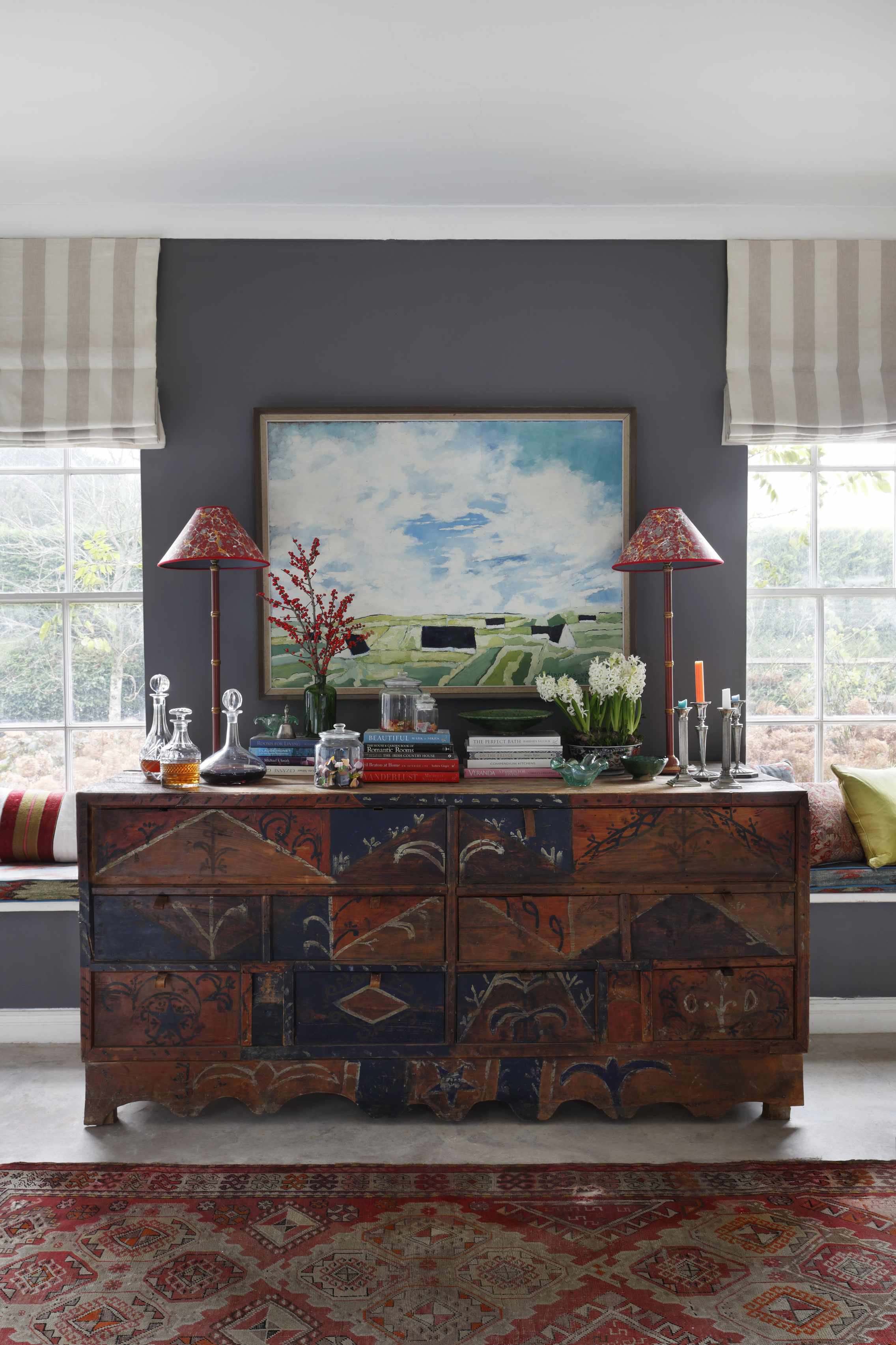 living room with grey accent, stripe blinds, vintage rug, console, window seats