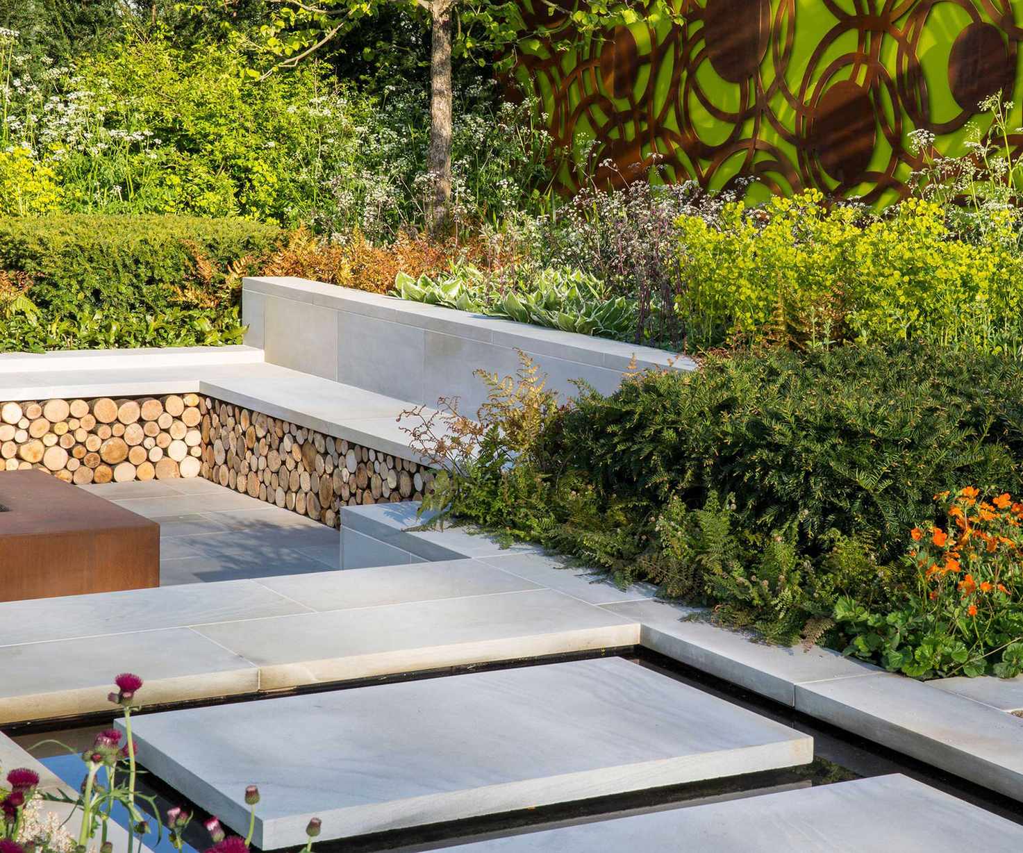 Yorkstone stepping stone slabs over a water feature leading to a sunken garden with stone bench and shrubs